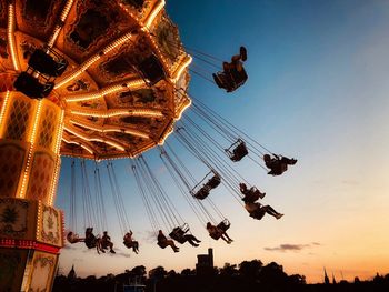 People on chain swing ride against sky during sunset