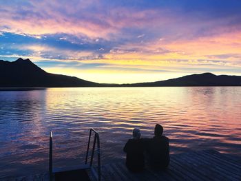 Silhouette people on lake against sky during sunset