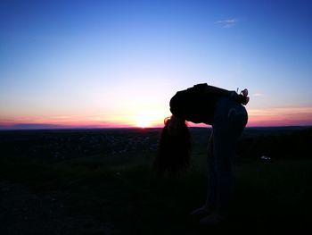 Silhouette woman photographing on field at sunset