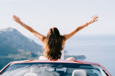 Rear view of woman with arms raised against sky