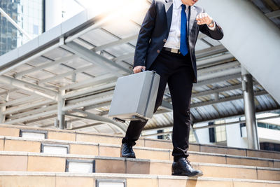 Low section of businessman holding briefcase while walking down steps in city