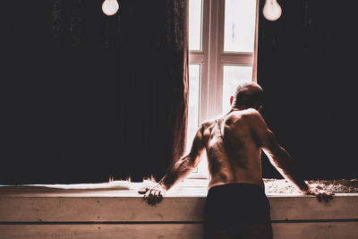 Full length of shirtless man lying in window
