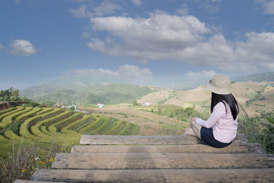 Woman sitting on landscape against sky