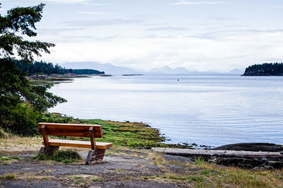 Bench by sea against sky