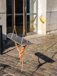 Rope swing over footpath against building during sunny day