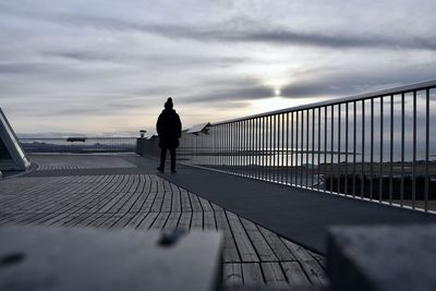 Rear view of man walking on bridge against sky