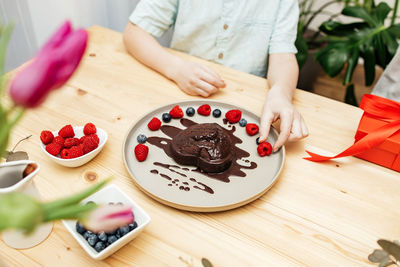 A boy decorates a heart-shaped chocolate cake for mother's day with fresh berries. valentine's day