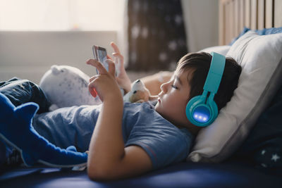 Young woman using mobile phone while lying on bed at home