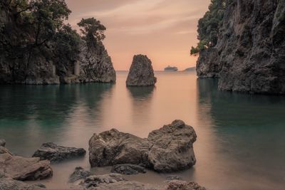 Rocks in sea against sky during sunset