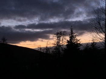 Silhouette of trees on landscape against cloudy sky