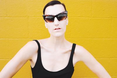 Young woman wearing sunglasses standing against yellow wall