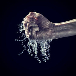 Close-up of wet human hand clenching fist against black background