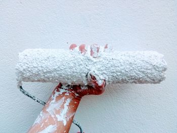 Close-up of hand holding paint roller against wall