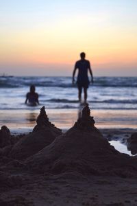 Silhouette people walking on beach against sky during sunset