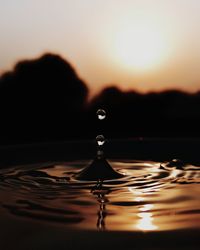 Close-up of drop falling on water against sky during sunset