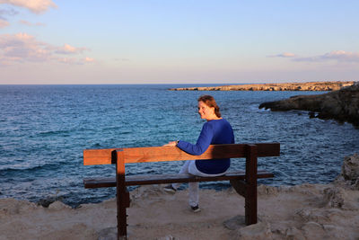 Rear view of man sitting on bench at beach