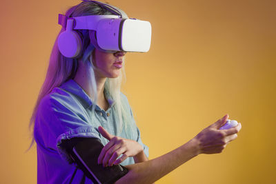 Woman wearing virtual reality simulator standing against yellow background