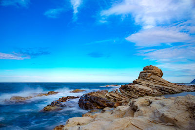 Rock formations on shore against blue sky