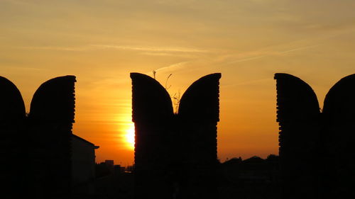 Silhouette built structure against orange sky