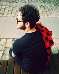 Rear view of man looking down while sitting on footpath