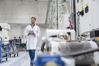 Employee checking manufacturing machines in high tech company, using digital tablet