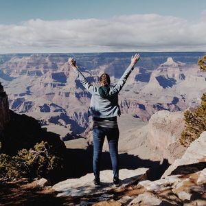 Full length rear view of woman with arms raised looking at mountains in desert