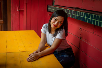 Portrait of young woman sitting against red wall