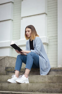 Low angle view of young woman reading book while sitting on sofa