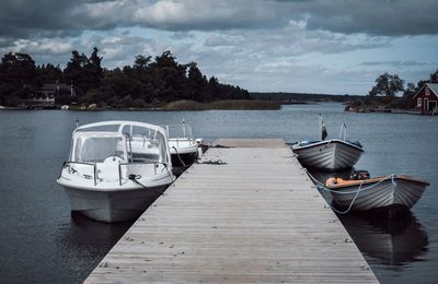 Boat moored on pier by lake against sky