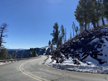 Road amidst trees against clear blue sky