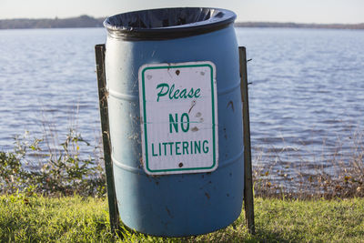 No littering sign on an empty garbage can on a lakeshore