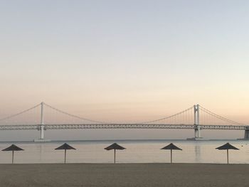 Suspension bridge over sea against sky during sunset