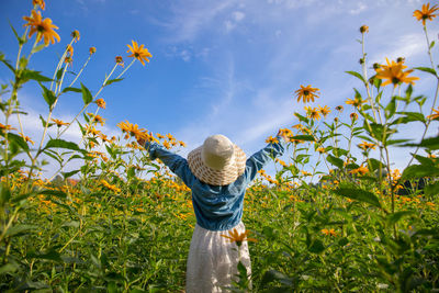 Rear view of girl standing by flowering plants against sky