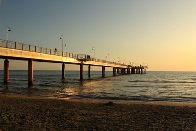 Pier on sea against clear sky at sunset