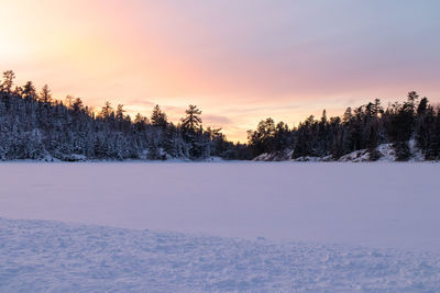 Snow covered field against sky at sunset