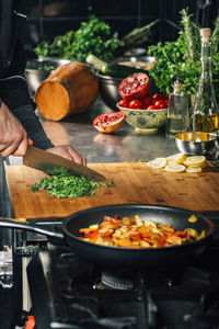 Chef holding a knife and cutting parsley on a wooden cutting board