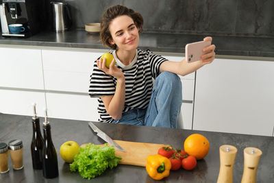Portrait of smiling young woman using mobile phone while sitting on table
