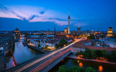 Illuminated city buildings by river against sky