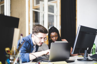 Young computer expert coding in laptop while working with female colleague at workplace