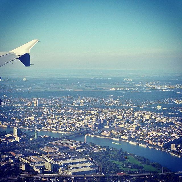 cityscape, city, aerial view, flying, architecture, built structure, building exterior, airplane, transportation, air vehicle, crowded, sea, sky, aircraft wing, mode of transport, high angle view, mid-air, blue, travel, residential district