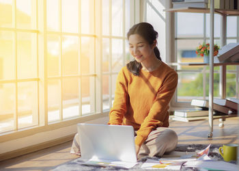 Full length of woman using mobile phone while sitting on table