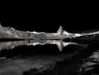 Scenic view of lake by snowcapped mountain against sky at night