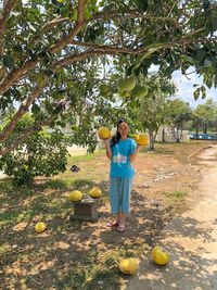 Full length portrait of woman holding fruits while standing by tree