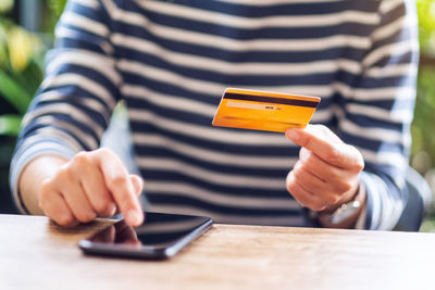 Closeup image of a young woman using credit card for purchasing and shopping online on mobile phone