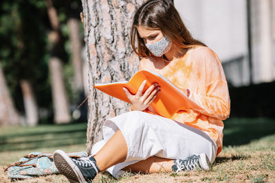 Side view of woman using phone while sitting on tree trunk