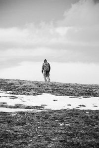 Scenic view of person on snow covered field against cloudy sky