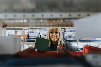 Portrait of smiling female worker taking equipment from shelf