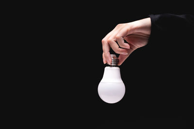 Cropped hand holding light bulb against black background