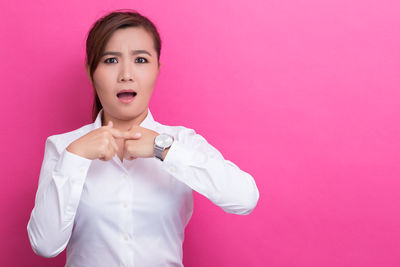 Portrait of young woman standing against pink background