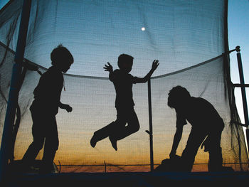 Silhouette boys playing against sky during sunset